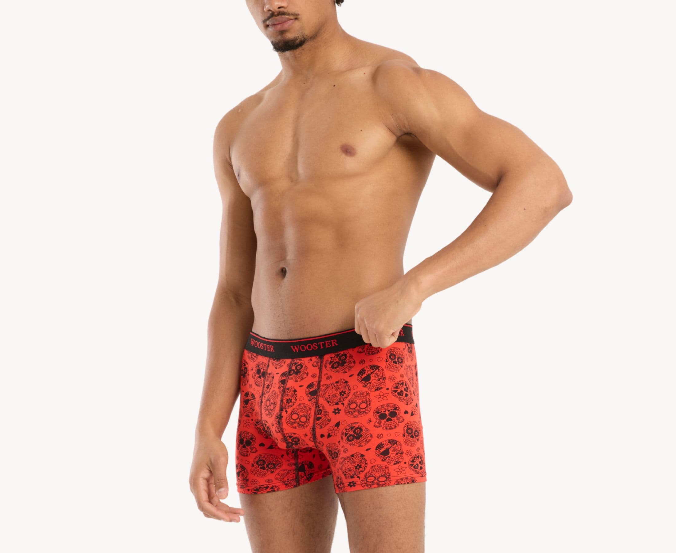 Side view of model wearing men’s 95% cotton crimson red boxer brief with black skulls in bloom print showing contoured pouch and relaxed fit