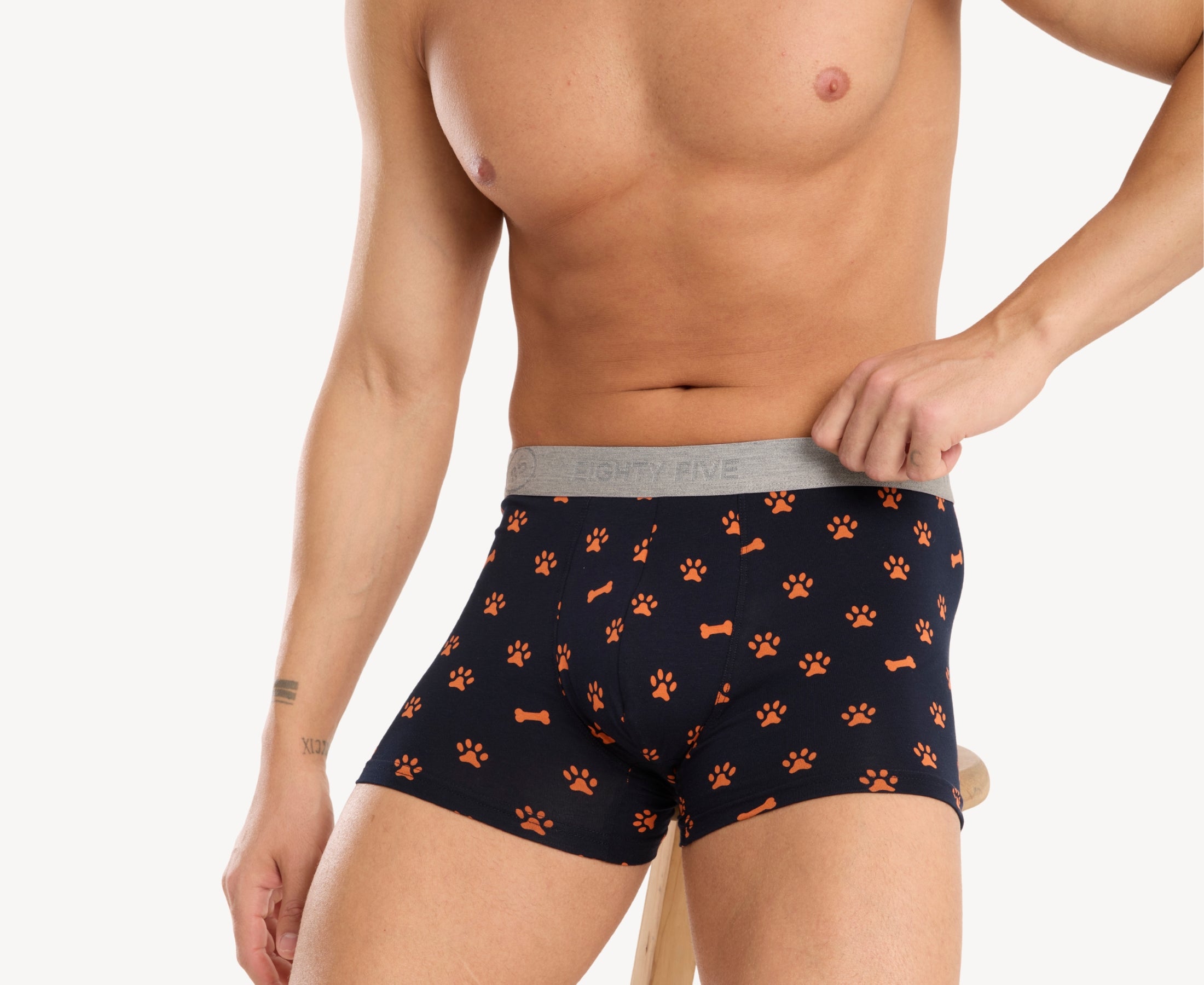 Front side view of male model wearing men’s 95% cotton boxer brief in navy with orange paws and bones print, showing smooth waistband and contoured fit