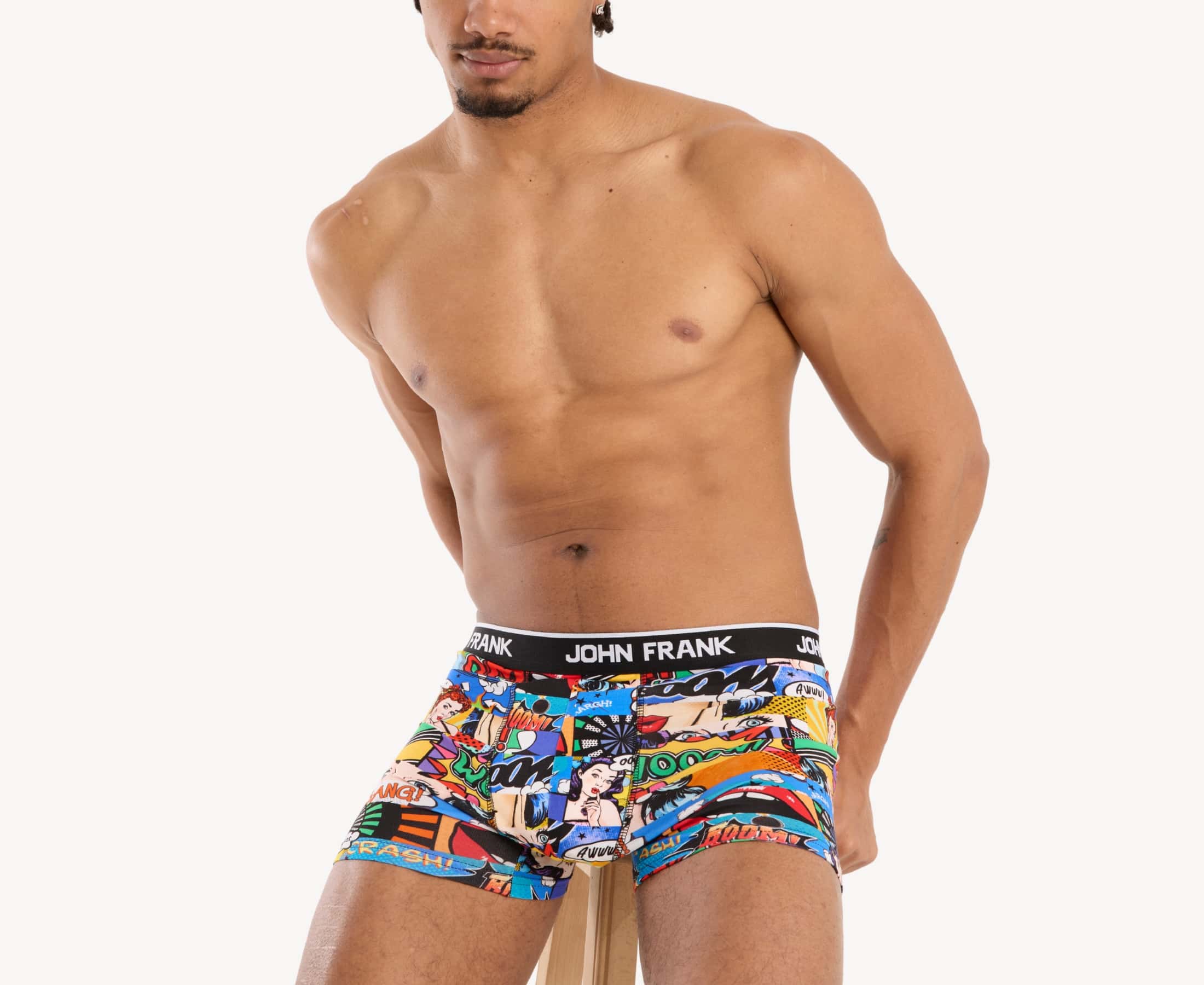 Seated view of model wearing men’s 95% cotton boxer brief in multicolor pop art print with smooth waistband and soft stretch fit