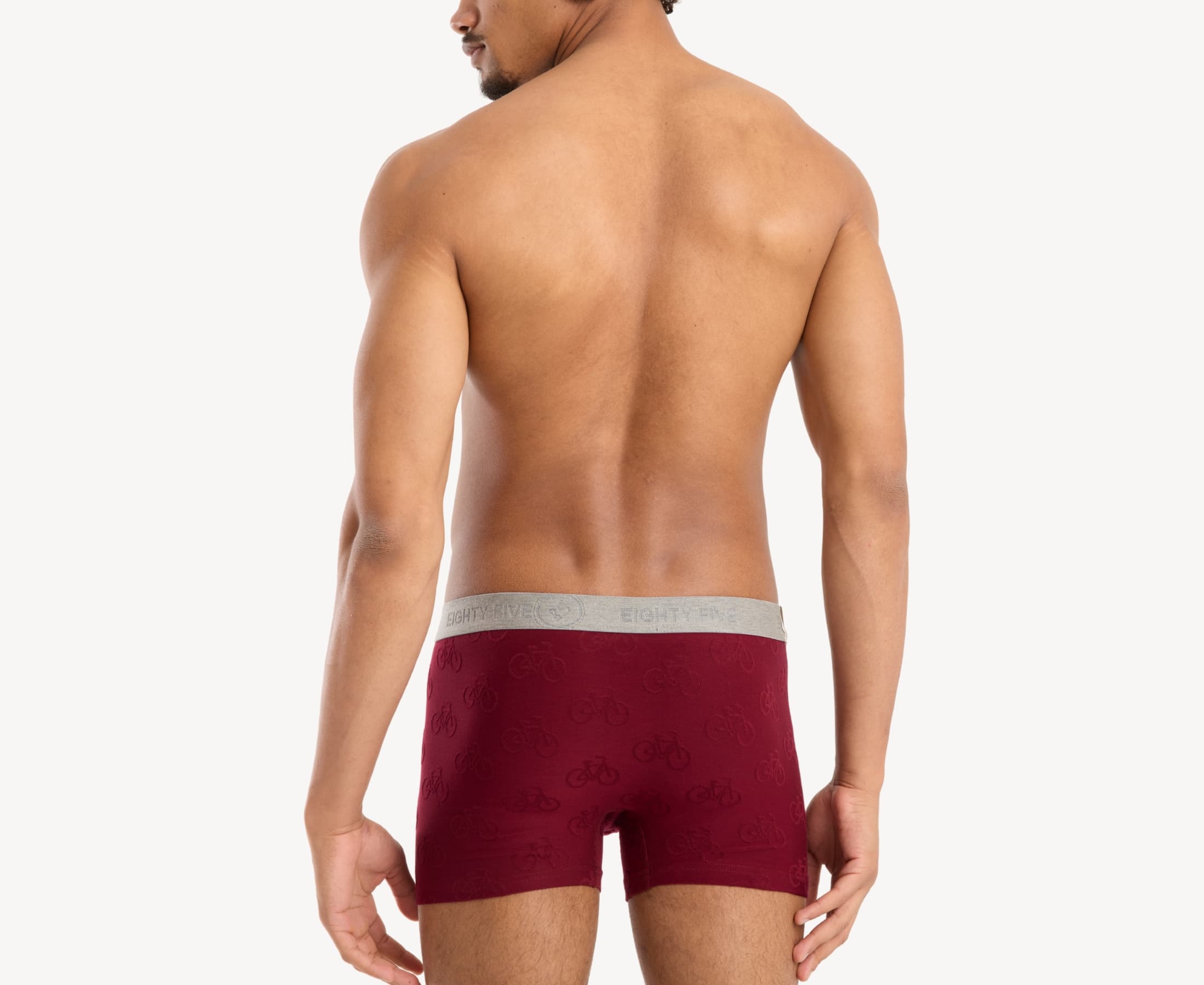 Back view of model wearing men’s 95% cotton boxer brief in burgundy with jacquard bicycles pattern, showcasing smooth waistband and rear detail