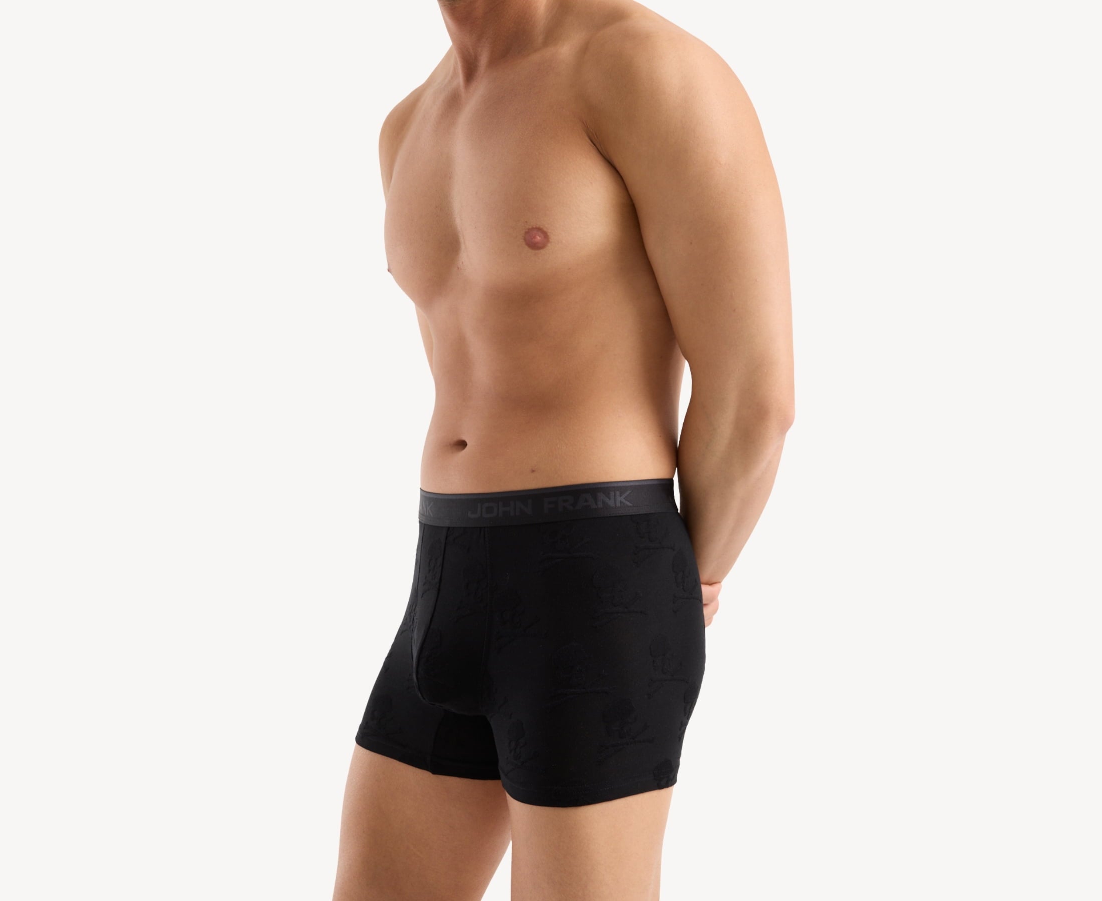 Side view of model wearing men’s 95% micromodal boxer brief in black with jacquard skull and cross bones pattern, showcasing contoured pouch, and tailored leg cut