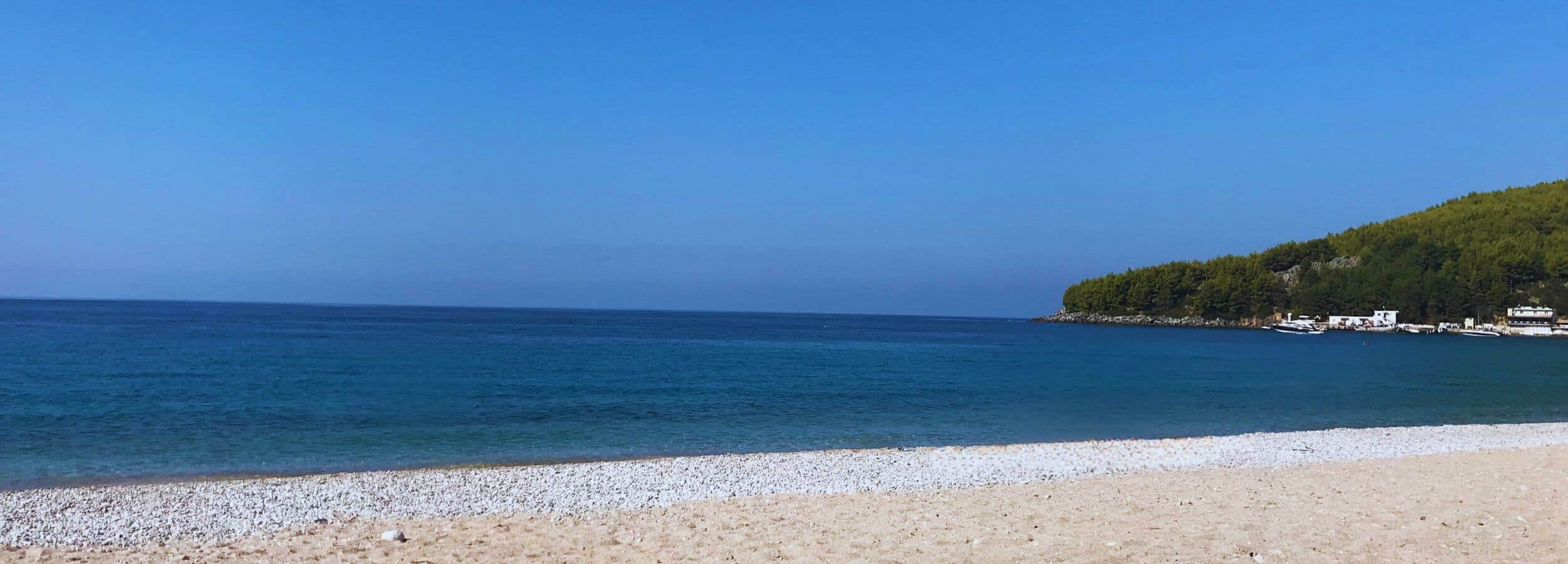 Peaceful beach scene with soft sand, calm waves, and a clear blue sky, used as background for Keççi’s homepage hero section