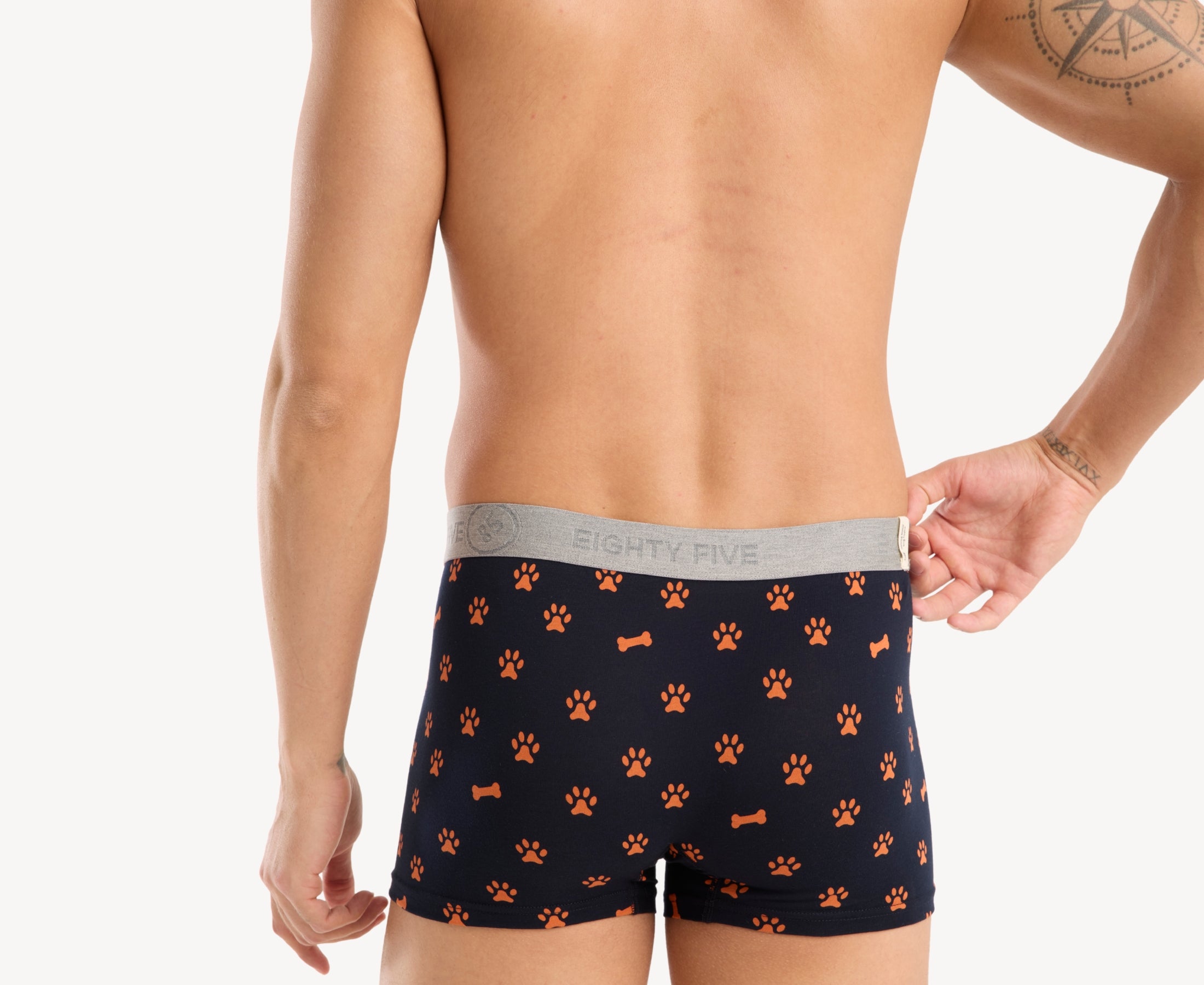 Back view of male model wearing men’s 95% cotton boxer brief in navy with orange paws and bones print, showing waistband detail