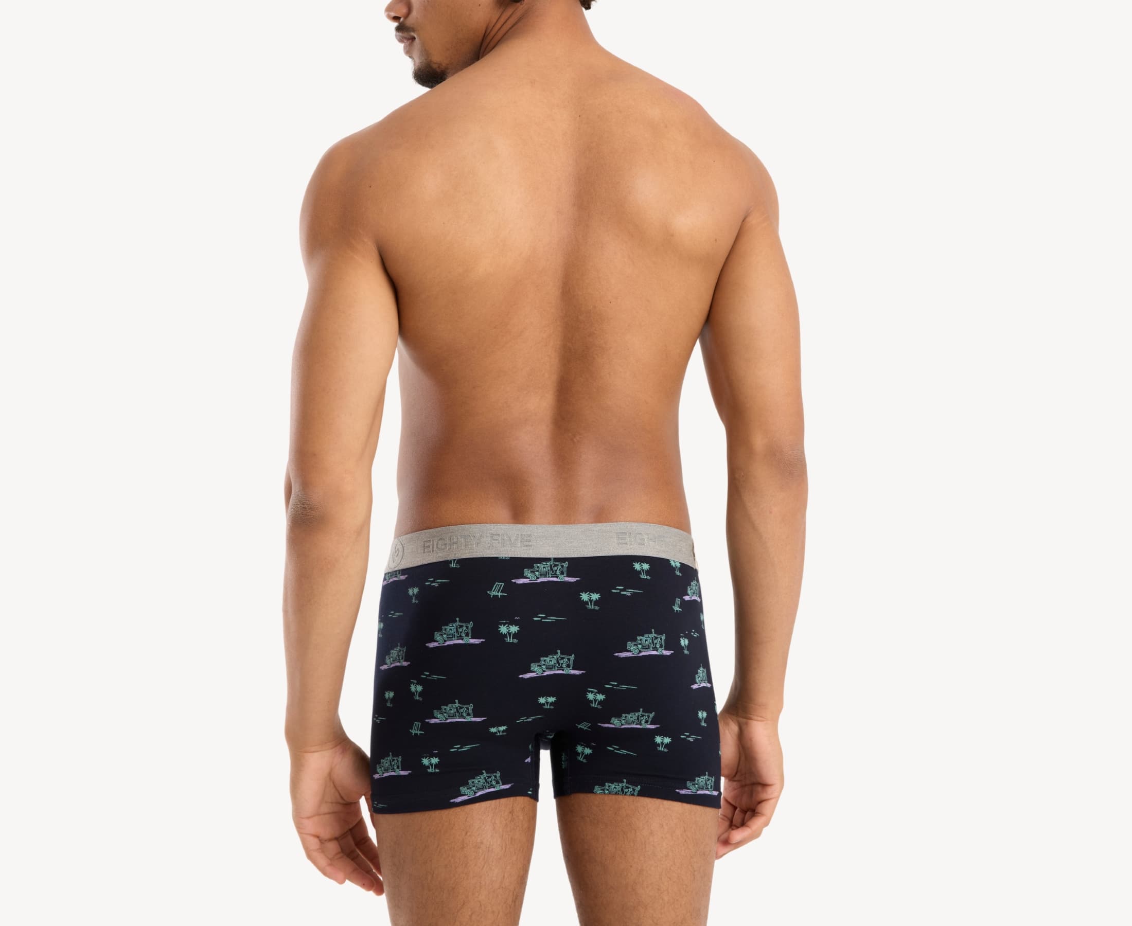 Back view of male model wearing men’s 95% cotton boxer brief in black with pink surf truck and green palms print, showing smooth waistband and contoured fit