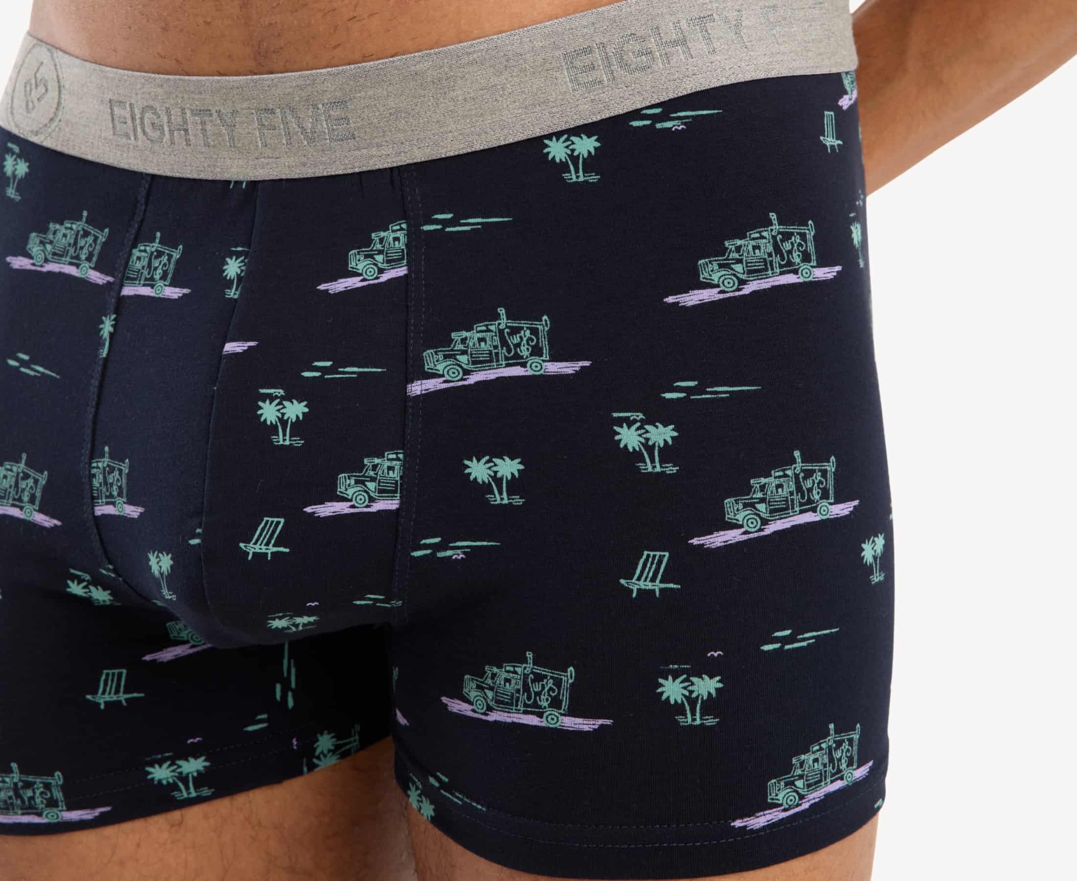 Close-up view of black with pink surf truck and green palms print and 'EIGHTY FIVE' branding on the gray waistband