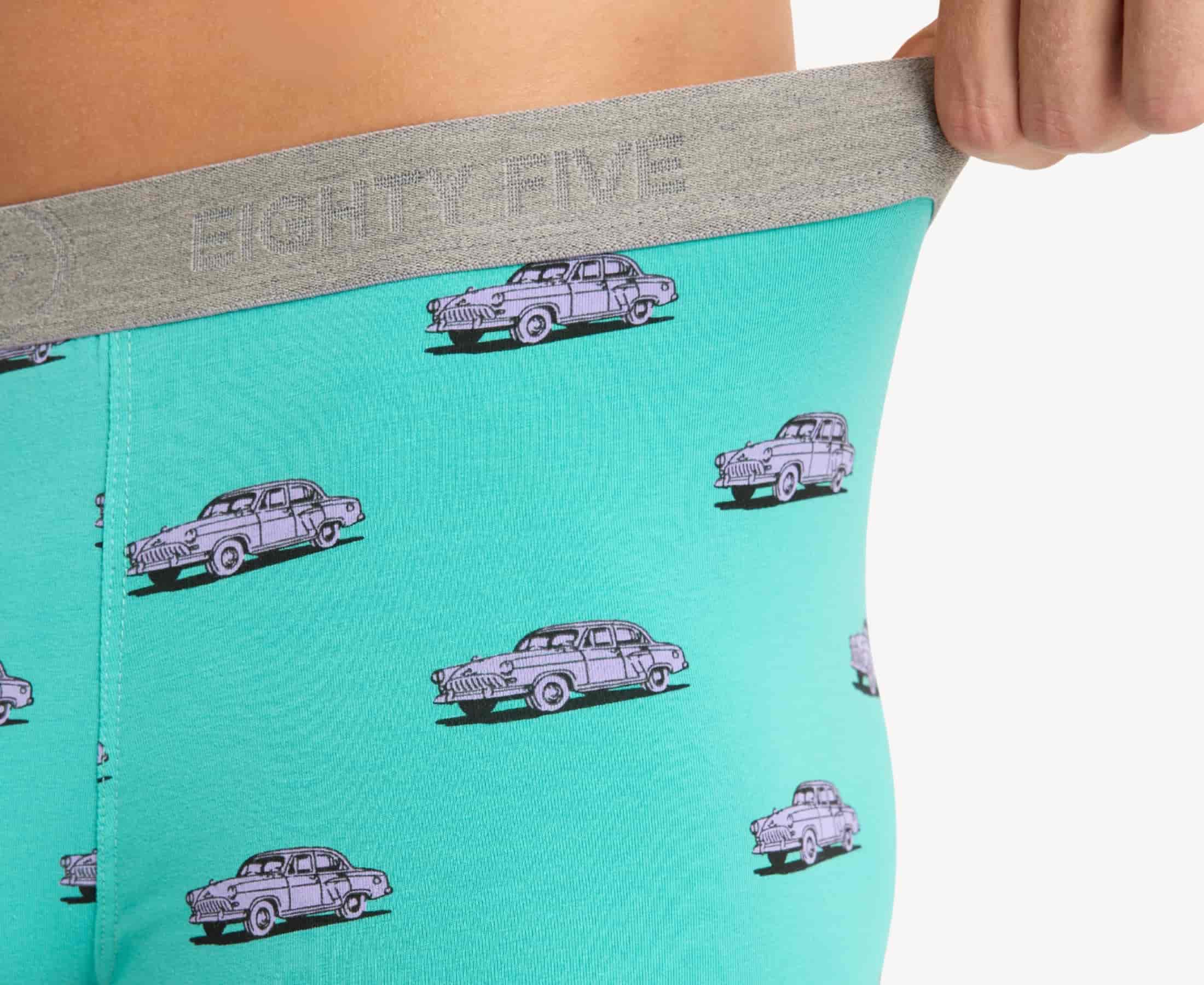 Close-up view of turquoise fabric with pink vintage car print and 'EIGHTY FIVE' branding on the gray  waistband