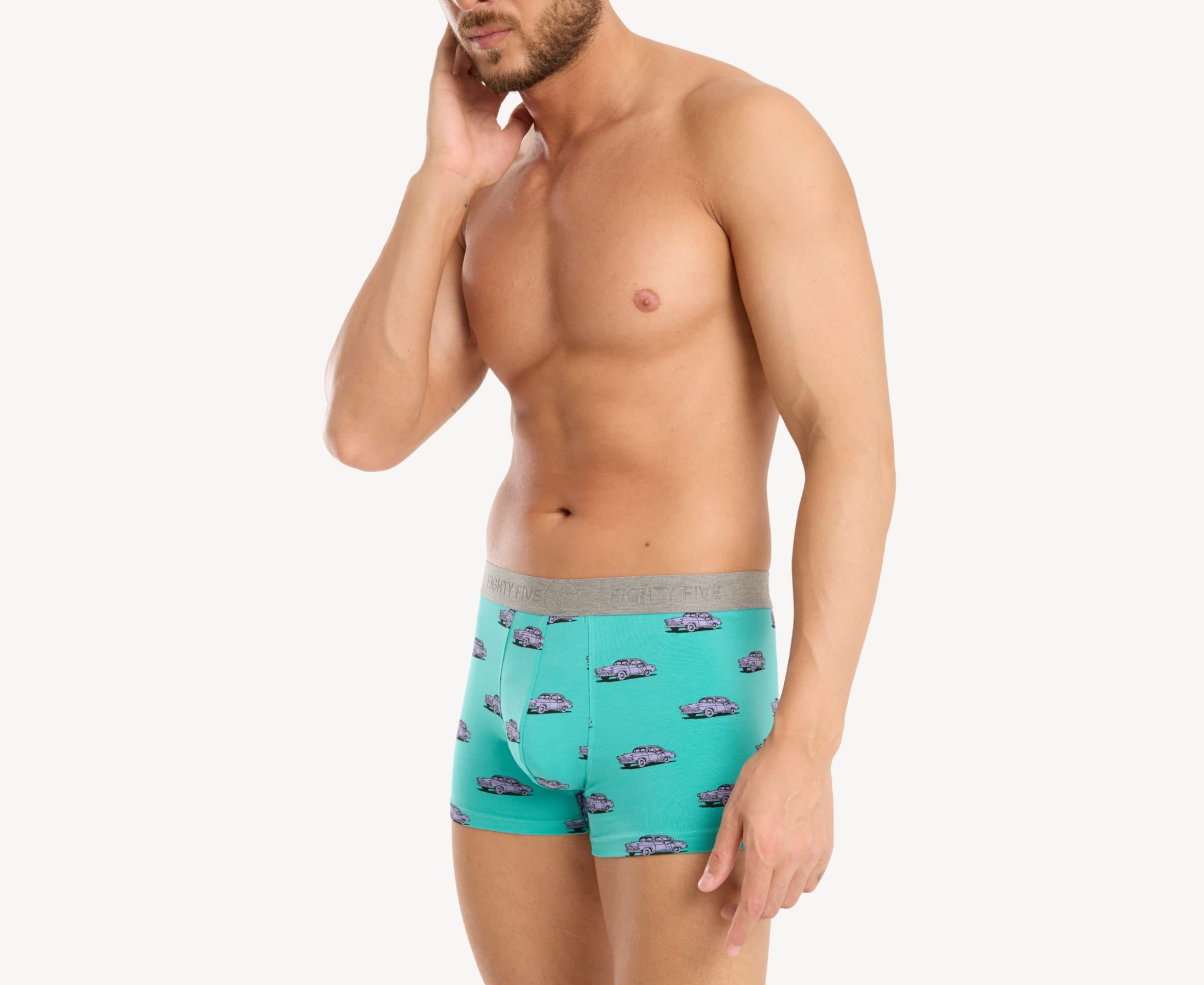 Quarter side view of male model wearing men’s 95% cotton boxer brief in turquoise with pink vintage car print, showing smooth waistband and natural fit through the leg